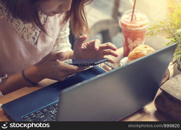 woman using smartphone in coffee shop with laptop