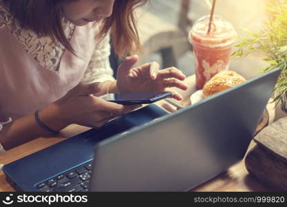 woman using smartphone in coffee shop with laptop