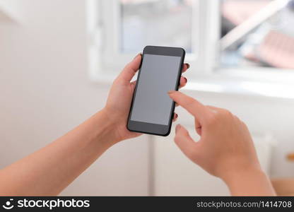 woman using smartphone office supplies technological devices inside home. Young lady using a dark smartphone inside home. Woman holding a black cell phone in a house ambient. Girl with technological devices and office supplies with blank space.