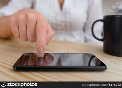 woman using smartphone office supplies technological devices inside home. Young lady using a dark smartphone inside home in a wooden desk. Woman touching a black cell phone with one finger in a house ambient. Girl with technological devices.