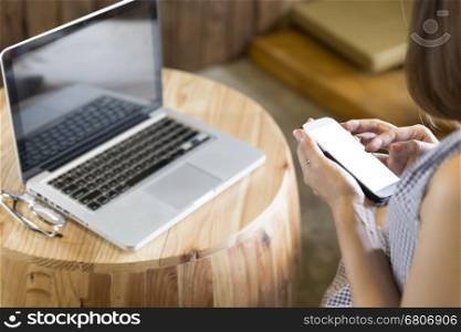 woman using smartphone with laptop computer notebook and eyeglasses on wooden desk