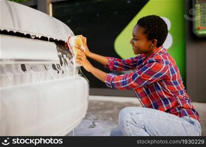 Woman using sponge and foam, hand auto wash station. Car-wash industry or business. Female person cleans her vehicle from dirt outdoors. Woman using sponge and foam, hand auto wash