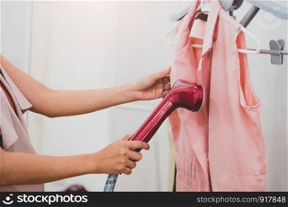 Woman using steaming iron to ironing fashion shirt in laundry room. Girl doing stream vapor iron for press clothes in hand. Launder concentrate work and delivery to customer. Part time job occupation