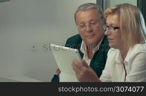 Woman using tablet, man drinking coffee and talking to woman. Both looking at pad.