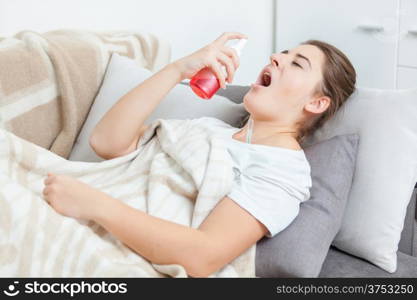 Woman using throat spray while lying on couch