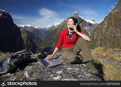 Woman using walkie-talkie and laptop on mountain peak