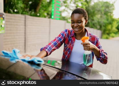 Woman using window cleaner spray, hand car wash station. Car-wash industry or business. Female person cleans her vehicle from dirt outdoors. Woman using window cleaner spray, hand car wash