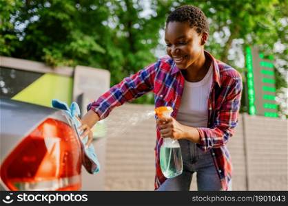 Woman using window cleaner spray, hand car wash station. Car-wash industry or business. Female person cleans her vehicle from dirt outdoors. Woman using window cleaner spray, hand car wash