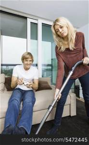 Woman vacuuming while man play video game in living room at home
