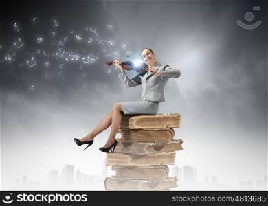 Woman violinist. Young businesswoman sitting on pile of books and playing violin