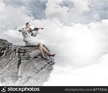 Woman violinist. Young businesswoman sitting on rock and playing violin