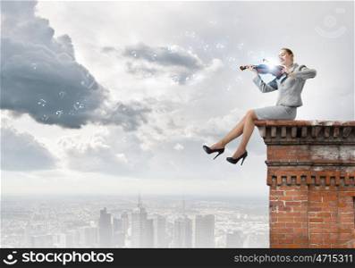 Woman violinist. Young businesswoman sitting on top of building and playing violin