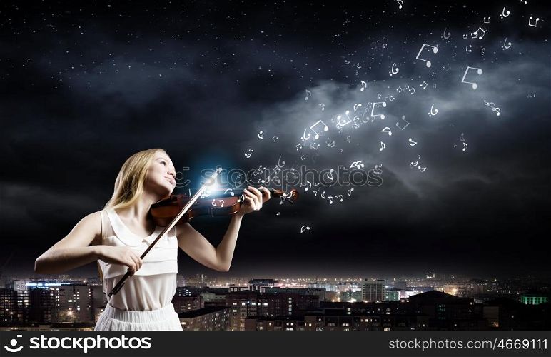 Woman violinist. Young woman in white dress playing violin at night