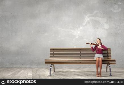 Woman violinist. Young woman sitting on bench and playing violin
