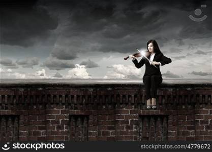 Woman violinist. Young woman sitting on building top and playing violin