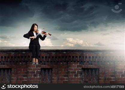 Woman violinist. Young woman sitting on building top and playing violin