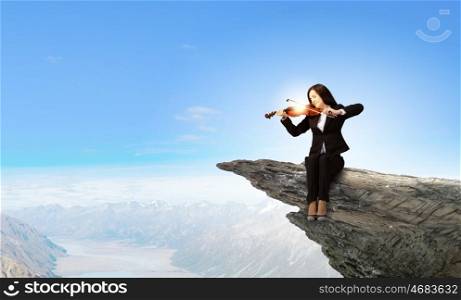 Woman violinist. Young woman sitting on cliff edge and playing violin