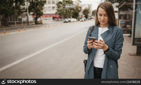 woman waiting bus searching her mobile phone