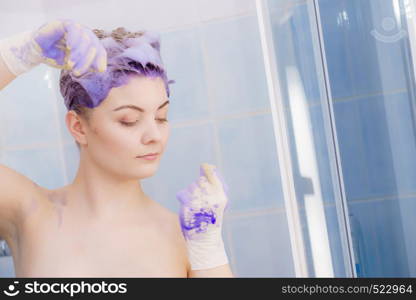 Woman waiting for coloring shampoo on her hair work. Female having purple washing product. Toning blonde color at home.. Woman applying toner shampoo on her hair