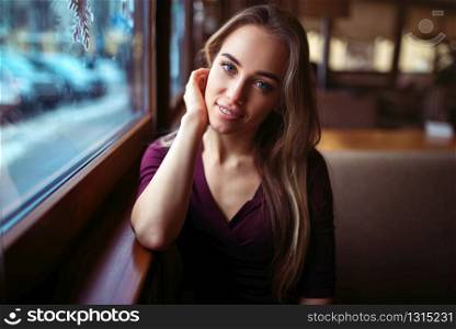 Woman waiting in cafe. Young girl sitting against the window and waiting for the order in restaurant.