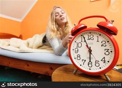 Woman waking up turning off alarm clock in morning. Woman waking up in bed turning off alarm clock. Young girl in the morning.