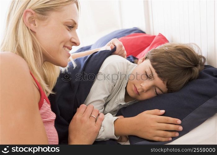 Woman waking young boy in bed smiling
