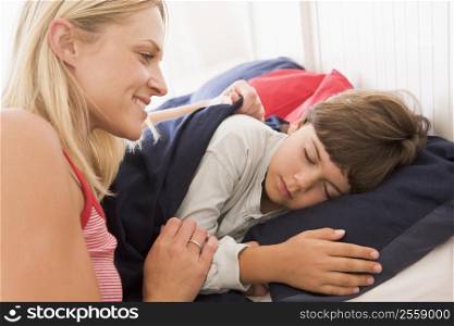 Woman waking young boy in bed smiling