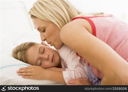 Woman waking young girl in bed with a kiss