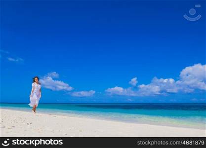 Woman walking along beach. Young woman in white dress walking along sand tropical beach