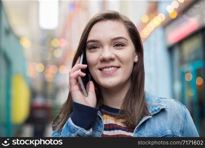 Woman Walking Along City Street Talking On Mobile Phone