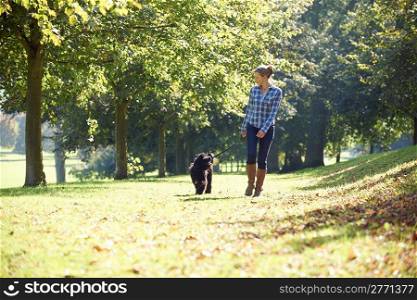 woman walking her black dog in the park on a sunny day