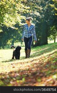 woman walking her black dog in the park on a sunny day