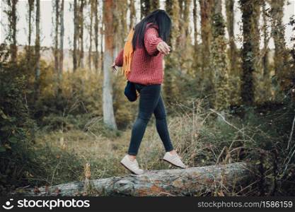 Woman walking on a trunk through the forest during the day wearing a yellow scarf and red wool jersey.. Woman walking on a trunk through the forest during the day