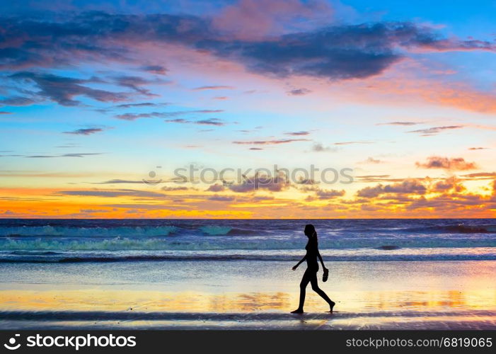 Woman walking on the beach at sunset barefooted with the shoes in her hand. Bali island, Indonesia