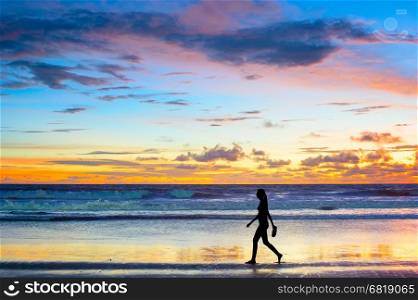 Woman walking on the beach at sunset barefooted with the shoes in her hand. Bali island, Indonesia