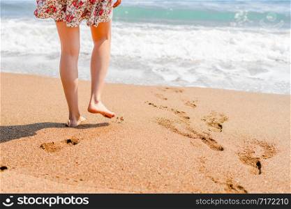 Woman walking on the beach to the sea in summer dress barefoot legs feet with footprints on the vacation holiday beach travel seashore ocean