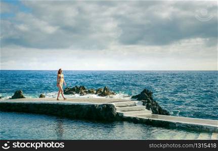 Woman walking on the pier in the ocean in cloudy day, Portugal, Madeira. Woman on a pier at the ocean