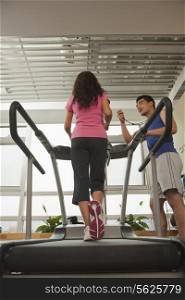 Woman walking on treadmill, trainer standing with stopwatch
