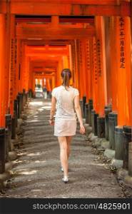 Woman walking through wooden Torii Gates at Fushimi Inari Shrine, Kyoto, Japan
