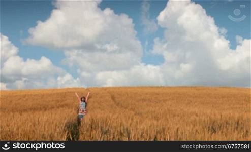 woman walks on a field of wheat against a blue sky