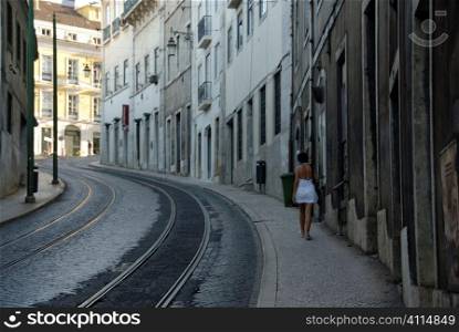 Woman walks uphill with Lisbon exteriors and tram lines