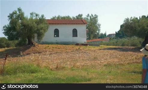 Woman wandering in the rural area with old building. She picking up the grass and walking away. Rustic landscape