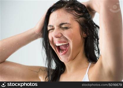 Woman washing her head while showering with happy smile and water splashing. Beautiful Caucasian female model home in shower cabin.