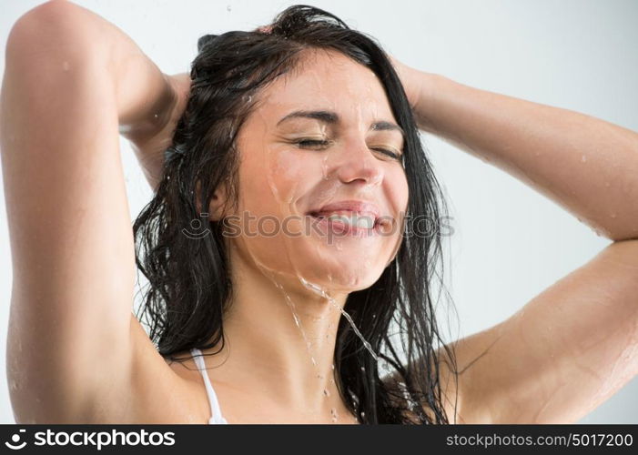 Woman washing her head while showering with happy smile and water splashing. Beautiful Caucasian female model home in shower cabin.