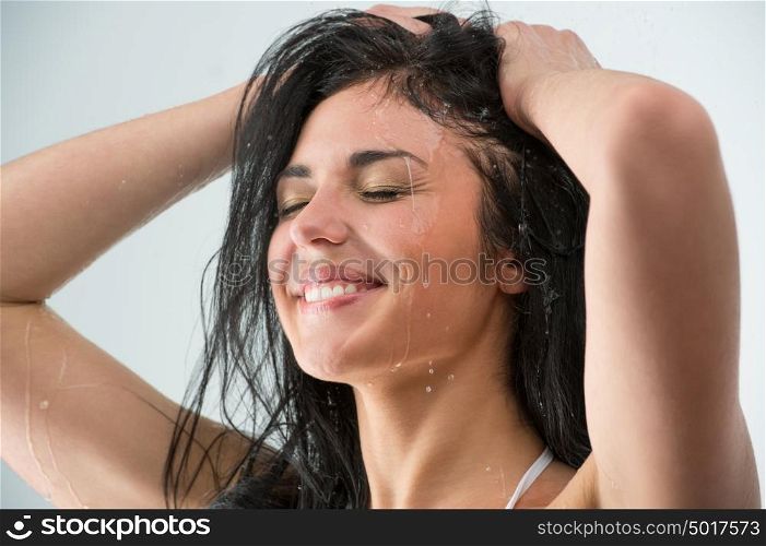 Woman washing her head while showering with happy smile and water splashing. Beautiful Caucasian female model home in shower cabin.