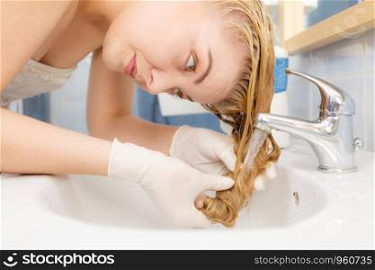 Woman washing her long blonde hair in bathroom sink. Hair care concept.. Woman washing her hair in sink