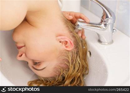 Woman washing her long blonde hair in bathroom sink. Haircare at home concept.. Woman washing hair in bathroom sink