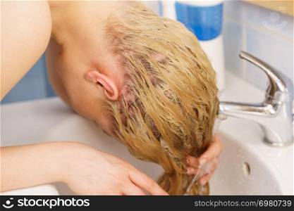 Woman washing her long blonde hair in bathroom sink. Haircare at home concept.. Woman washing hair in bathroom sink