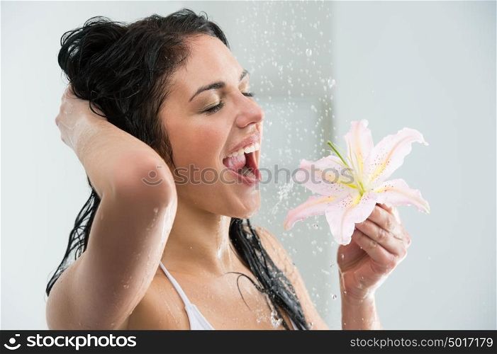 Woman washing herself while showering with happy smile, lily flower and water splashing. Beautiful Caucasian female model on vacation at hotel in shower cabin.