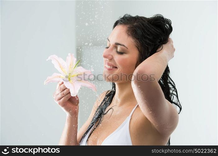 Woman washing herself while showering with happy smile, lily flower and water splashing. Beautiful Caucasian female model on vacation at hotel in shower cabin.